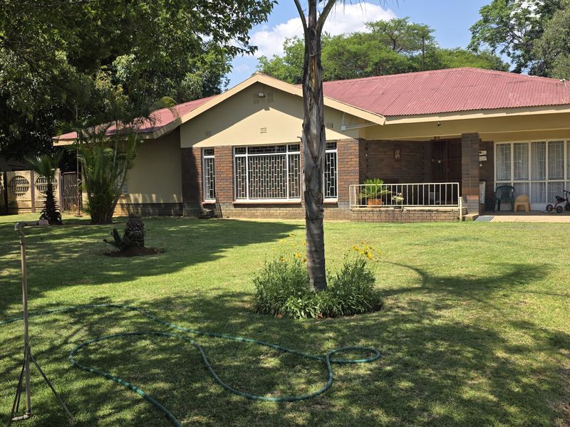 Front view of a single-story residence featuring a corrugated metal roof, brick exterior, covered patio, and a spacious front lawn with a carport.