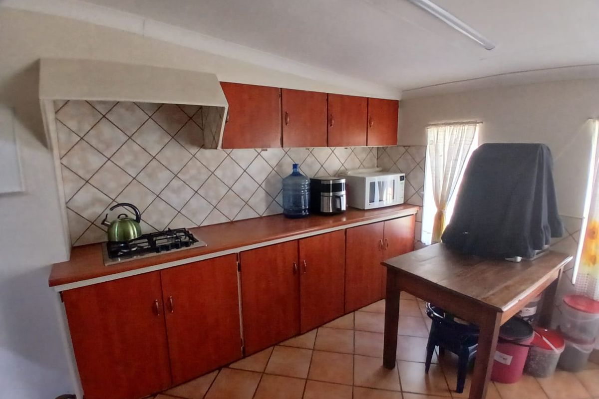 A functional kitchen featuring wooden cabinetry, a gas hob with extractor hood, tiled backsplash, and tiled flooring.