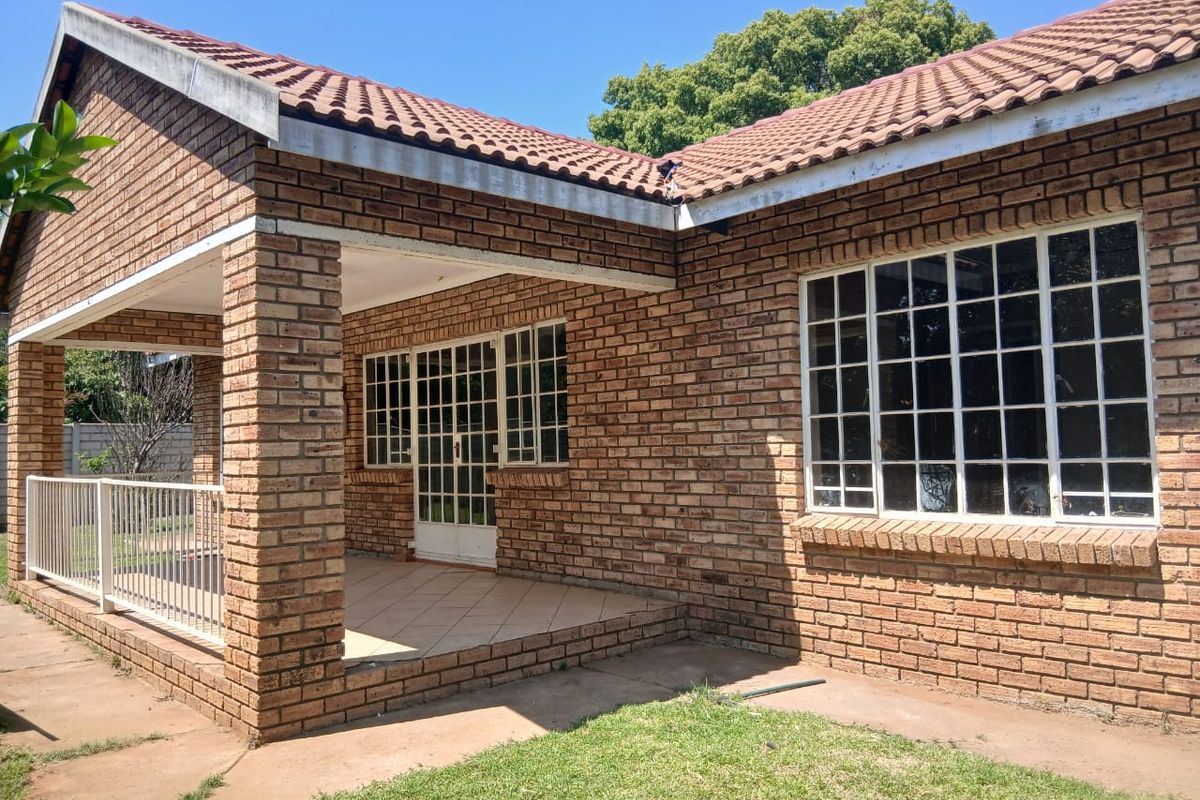 A rear view of the face brick property featuring a covered patio area with tiled flooring and steel-framed windows.