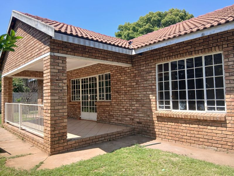 A rear view of the face brick property featuring a covered patio area with tiled flooring and steel-framed windows.