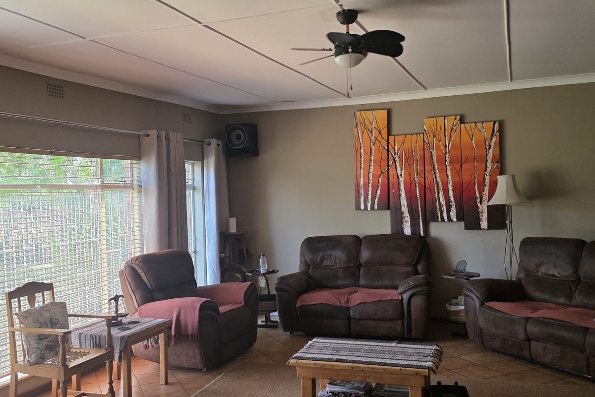 A comfortable living room featuring tiled flooring, a ceiling fan, and large windows that provide ample natural light.