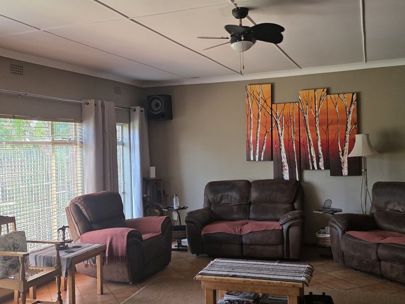 A comfortable living room featuring tiled flooring, a ceiling fan, and large windows that provide ample natural light.