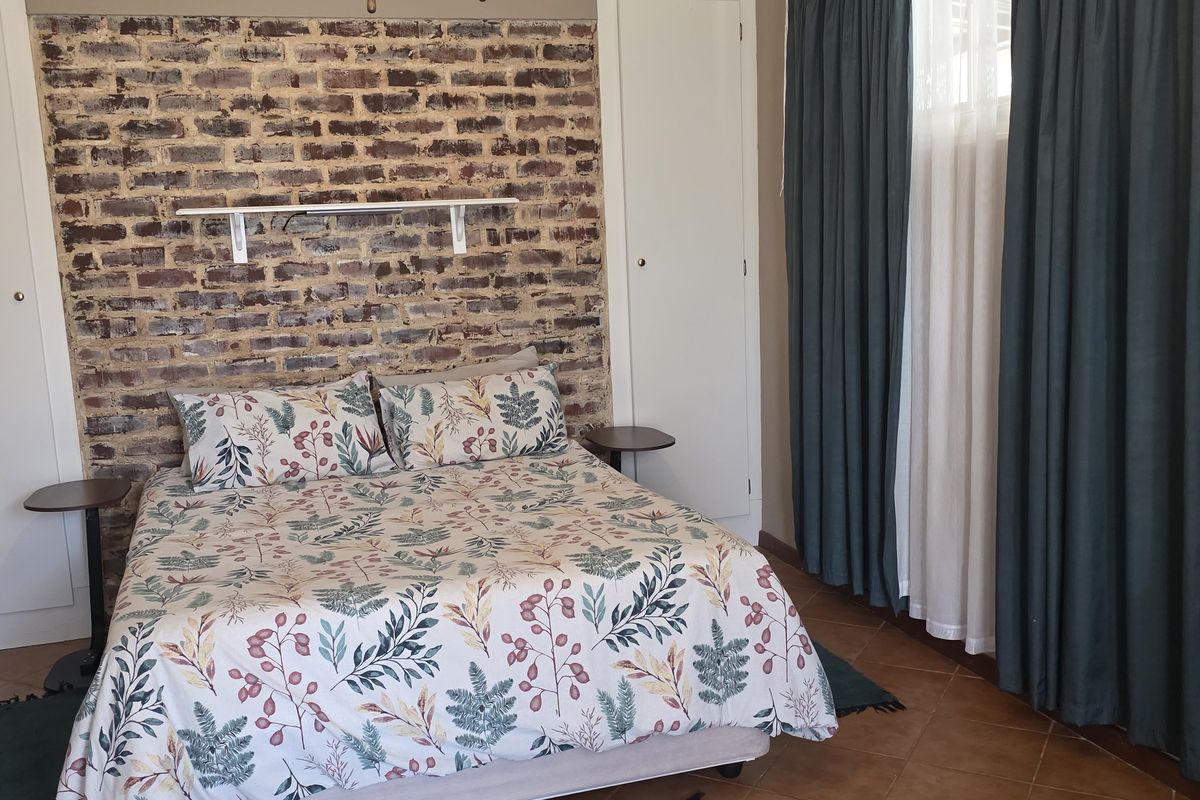 A bedroom featuring an exposed brick accent wall, built-in cupboards, and tiled flooring, offering a rustic aesthetic.