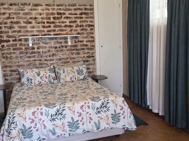 A bedroom featuring an exposed brick accent wall, built-in cupboards, and tiled flooring, offering a rustic aesthetic.