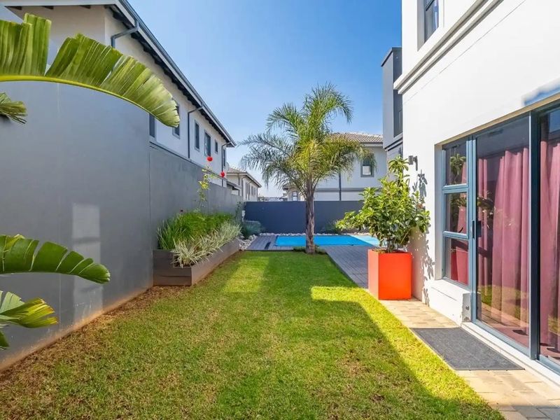 A well-maintained rear garden featuring a manicured lawn, a swimming pool, paved patio area, and modern boundary walls with integrated planters.