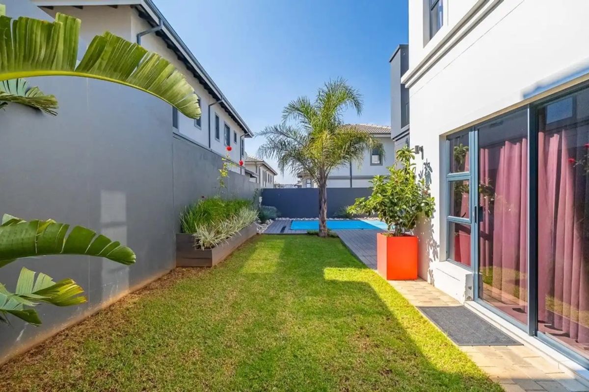 A well-maintained rear garden featuring a manicured lawn, a swimming pool, paved patio area, and modern boundary walls with integrated planters.