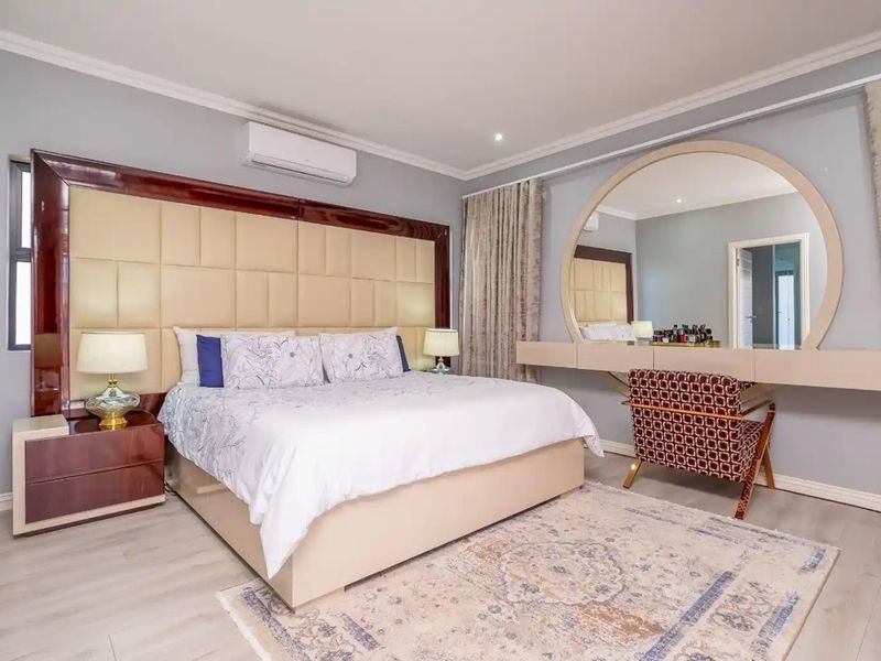 Spacious bedroom featuring a large built-in headboard, integrated vanity area with circular mirror, wall-mounted air conditioning, and modern laminate flooring.