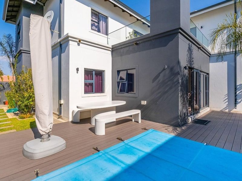 A well-maintained outdoor pool area featuring composite decking, a swimming pool with cover, and modern architectural finishes including a glass balustrade.