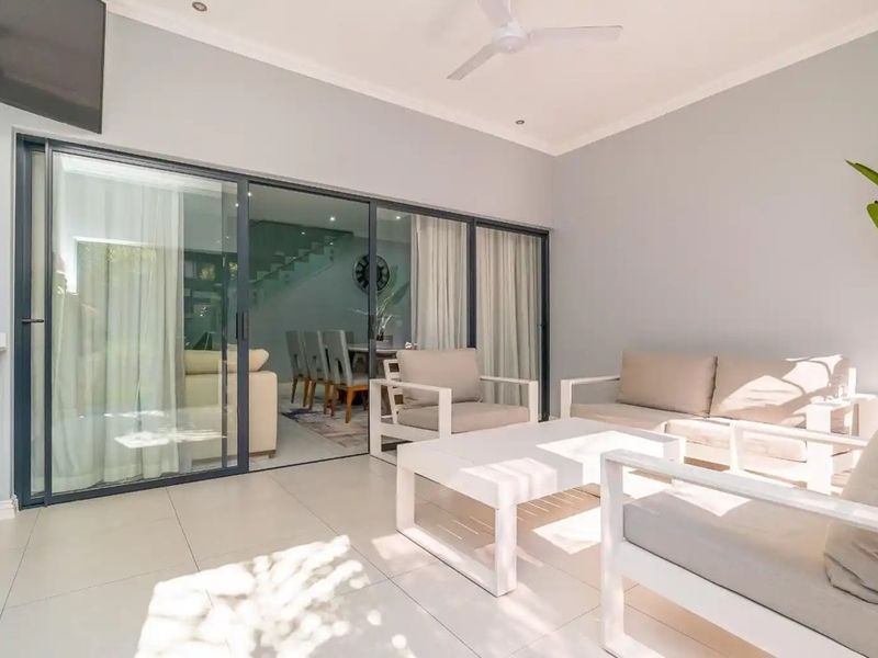 A modern covered patio featuring large sliding glass doors, tiled flooring, a ceiling fan, and built-in cabinetry, seamlessly connecting to the indoor living area.