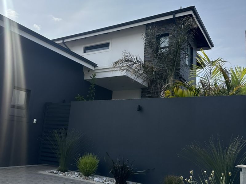 Modern cluster home exterior featuring a paved driveway, contemporary dark facade, and stone-clad architectural detailing with landscaped garden beds.