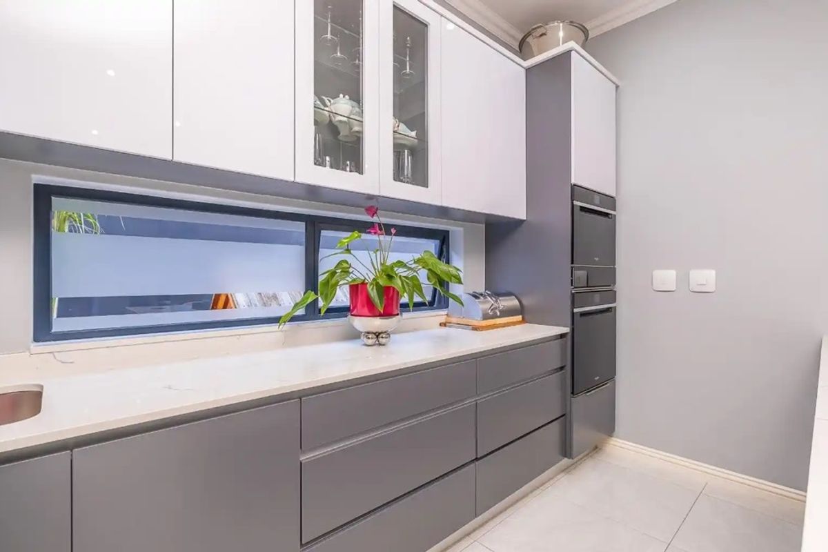 Modern kitchen featuring sleek grey and white cabinetry, stone countertops, integrated appliances, and a horizontal window providing natural light.