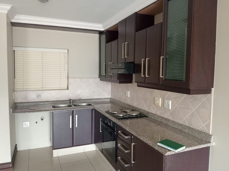 A functional kitchen featuring dark wood cabinetry, granite countertops, built-in oven and hob, and a tiled backsplash with neutral finishes.