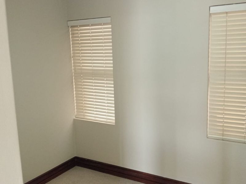 A clean, empty bedroom featuring neutral wall paint, carpeted flooring, crown molding, and fitted venetian blinds on the windows.