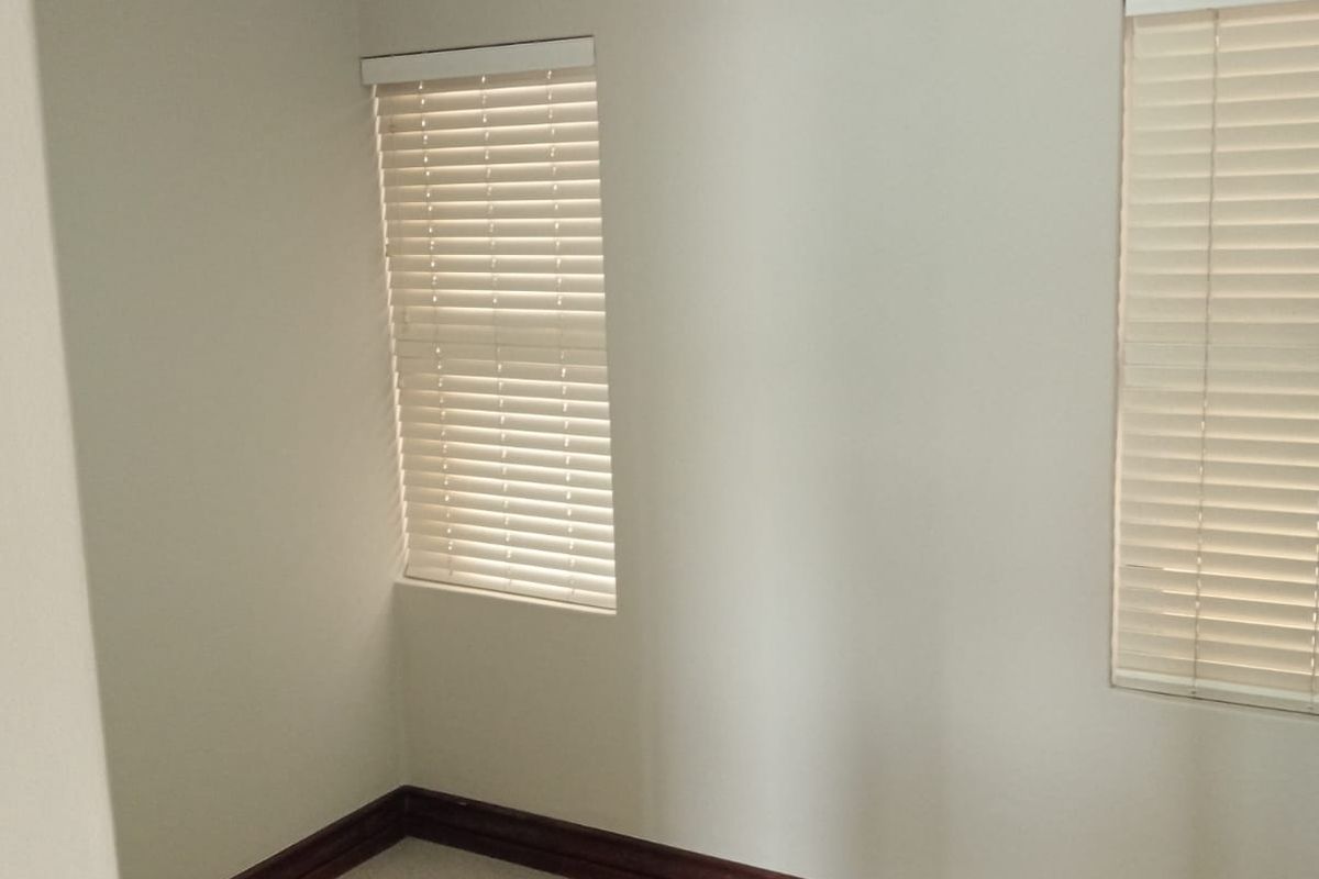 A clean, empty bedroom featuring neutral wall paint, carpeted flooring, crown molding, and fitted venetian blinds on the windows.