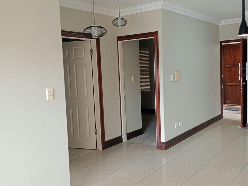 A bright and spacious hallway featuring neutral walls, tiled flooring, and classic coving, providing access to multiple rooms within the apartment.
