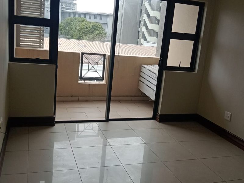 An empty living room featuring neutral tiled flooring, dark skirting boards, and a large sliding glass door providing access to a private balcony.