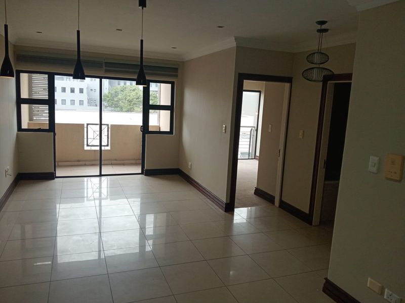 Spacious, light-filled living area featuring polished tile flooring, modern pendant lighting, and direct access to a private balcony through sliding glass doors.