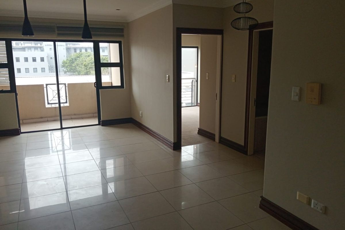 An open-plan living area featuring neutral tiled flooring, recessed lighting, and direct access to a private balcony through sliding glass doors.