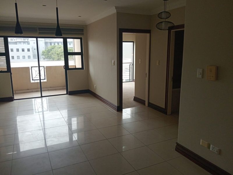 An open-plan living area featuring neutral tiled flooring, recessed lighting, and direct access to a private balcony through sliding glass doors.