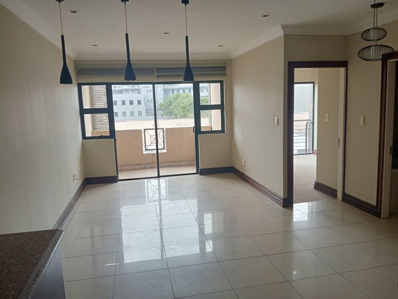 An open-plan living area featuring polished porcelain floor tiles, recessed lighting, and a sliding glass door leading to a private balcony.