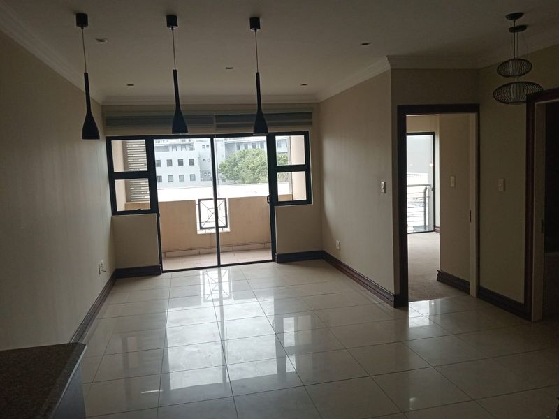 Spacious, open-plan living area featuring polished tile flooring, modern pendant lighting, and direct access to a private balcony through sliding glass doors.