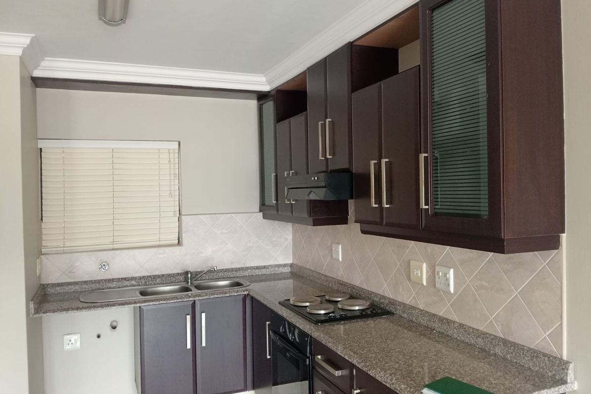 A functional kitchen featuring dark wood cabinetry, granite countertops, a built-in oven, and an electric hob with a tiled backsplash.