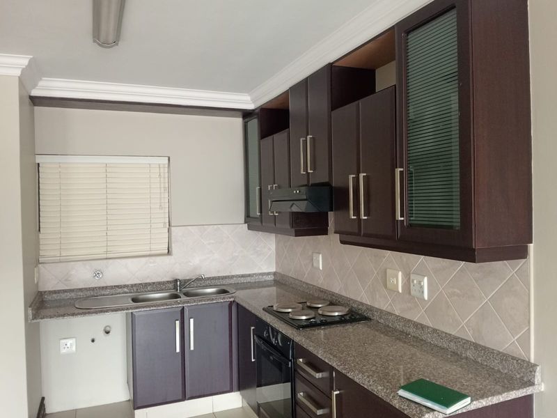 A functional kitchen featuring dark wood cabinetry, granite countertops, a built-in oven, and an electric hob with a tiled backsplash.