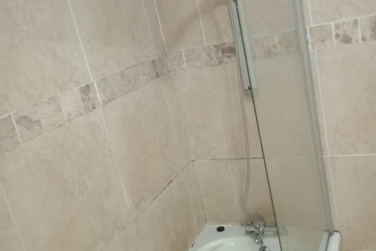 A bathroom featuring a bathtub with a glass shower screen and neutral wall tiling.