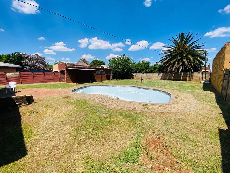 Spacious backyard featuring a swimming pool with brick surround, a covered patio area, and perimeter boundary walls.