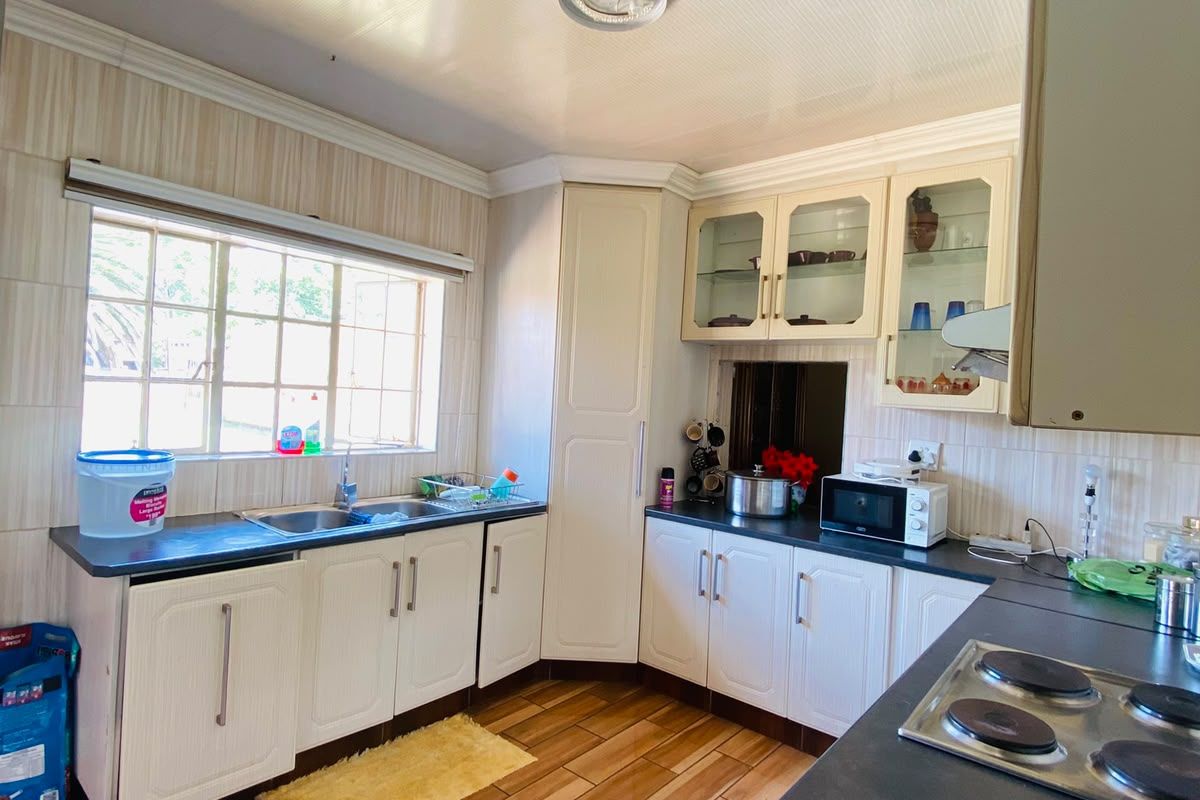 A functional kitchen featuring built-in cabinetry, laminate countertops, a stainless steel sink, and an electric hob with tiled flooring and backsplash.