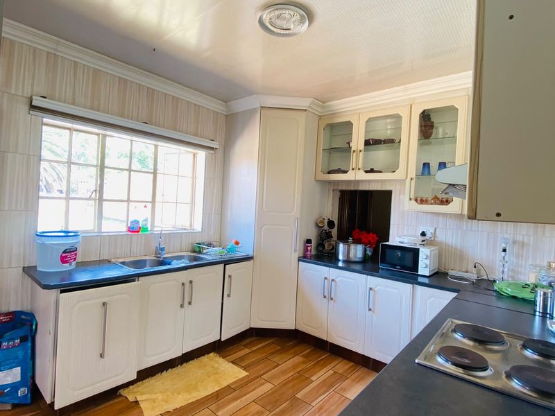 A functional kitchen featuring built-in cabinetry, laminate countertops, a stainless steel sink, and an electric hob with tiled flooring and backsplash.