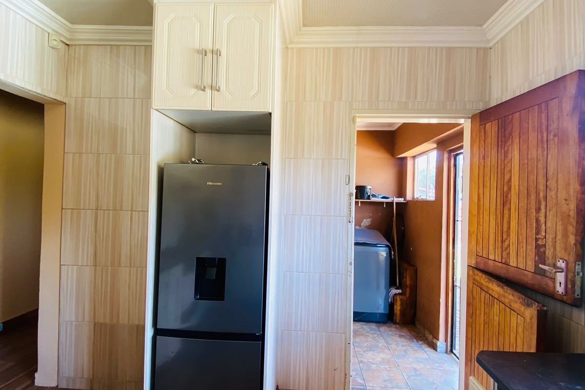 Kitchen area featuring built-in cabinetry, crown molding, and tiled finishes, with an adjacent utility space visible through the doorway.