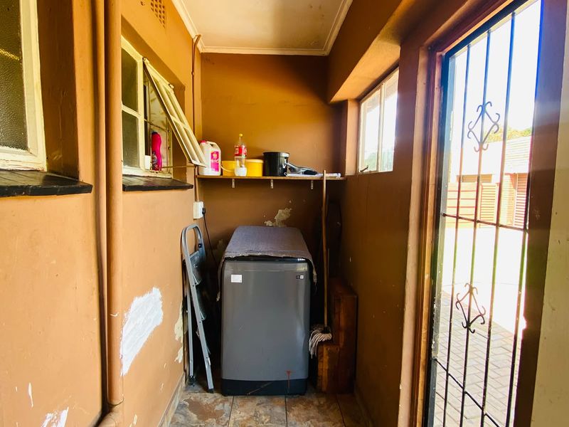 A functional laundry area featuring tiled flooring, security gate access, and built-in shelving, requiring some maintenance to the ceiling and wall finishes.