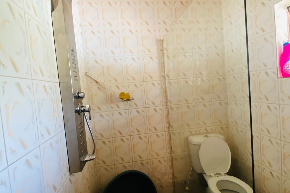 A compact bathroom featuring a modern stainless steel shower panel, glass screen, and standard toilet with tiled finishes throughout.