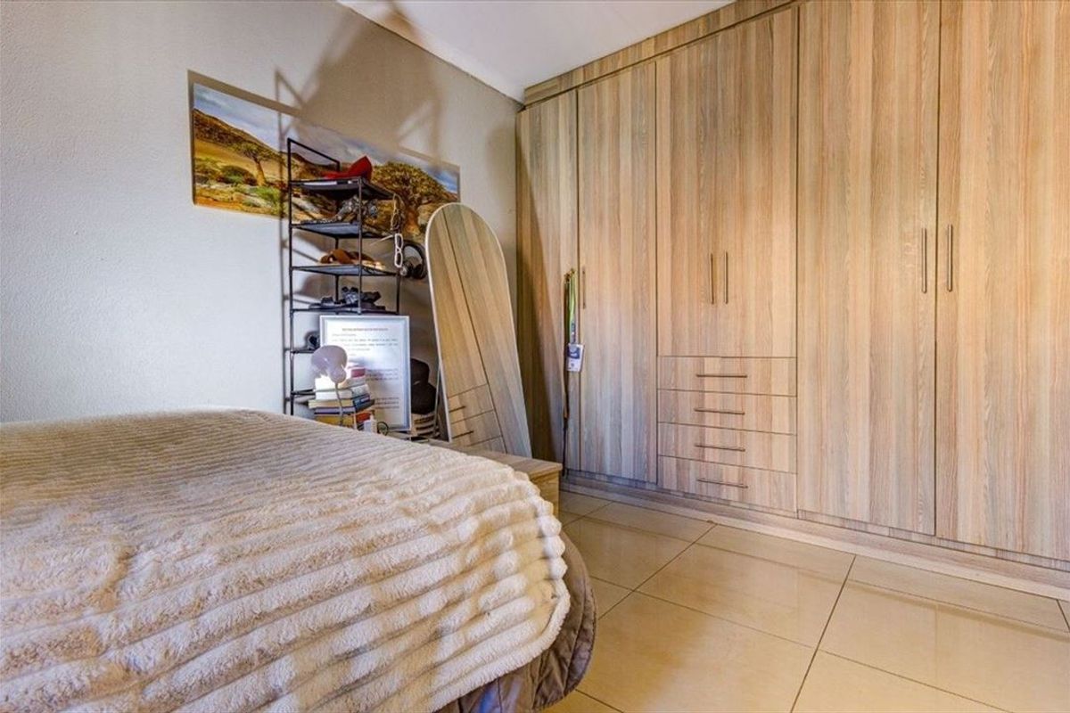A well-maintained bedroom featuring extensive built-in wooden cabinetry and neutral tiled flooring.