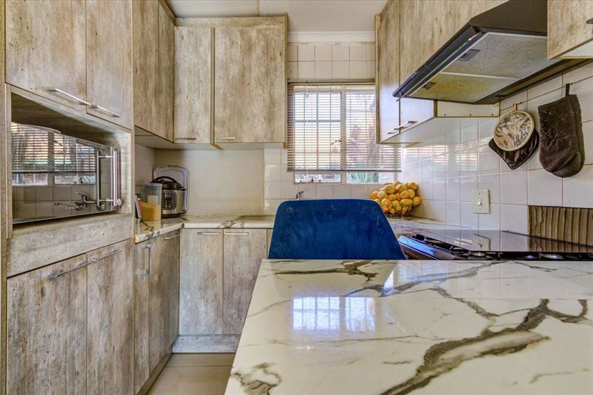 Compact kitchen featuring wood-look cabinetry, marble-effect countertops, tiled backsplash, and integrated appliances, offering a functional layout with natural light.
