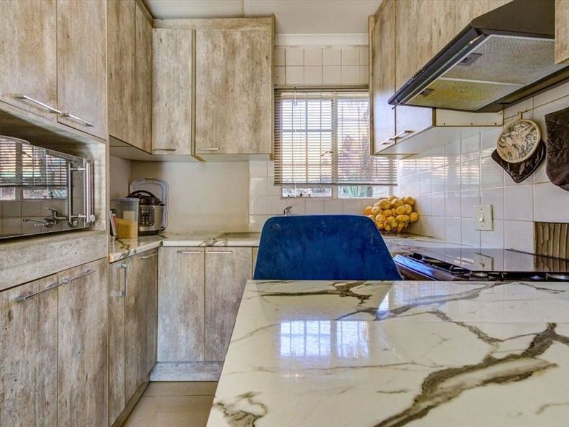 Compact kitchen featuring wood-look cabinetry, marble-effect countertops, tiled backsplash, and integrated appliances, offering a functional layout with natural light.