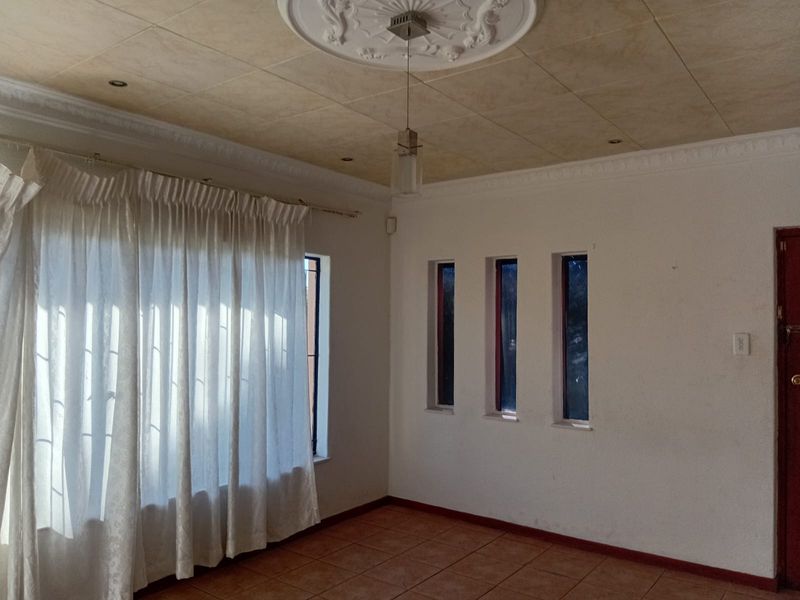 An empty living room featuring tiled flooring, decorative ceiling rose, cornice detailing, and multiple vertical windows providing natural light.