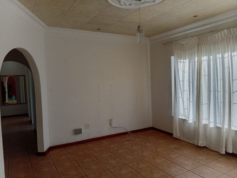 An empty living room featuring tiled flooring, an arched entryway, and decorative ceiling coving with a central rose.