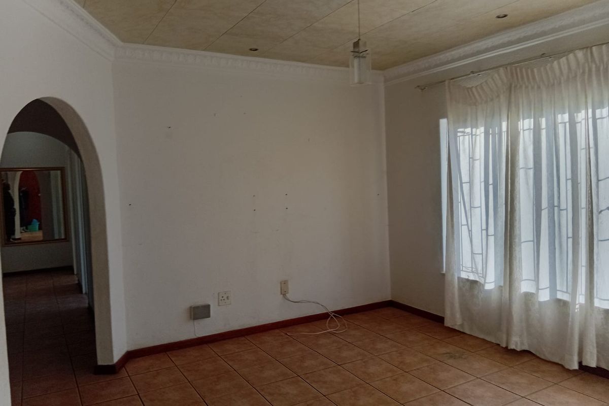 An empty living room featuring tiled flooring, an arched entryway, and decorative ceiling coving with a central rose.