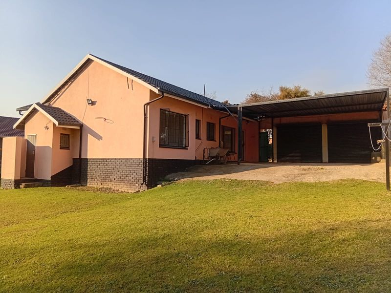 Rear view of the house featuring a tiled roof, brick plinth, security bars on windows, and a covered carport with roller shutter garage doors.