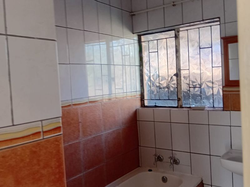 A dated bathroom featuring a built-in bathtub, wall-mounted basin, and two-tone tiled walls with security bars on the window.
