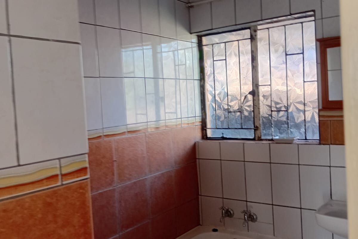 A dated bathroom featuring a built-in bathtub, wall-mounted basin, and two-tone tiled walls with security bars on the window.