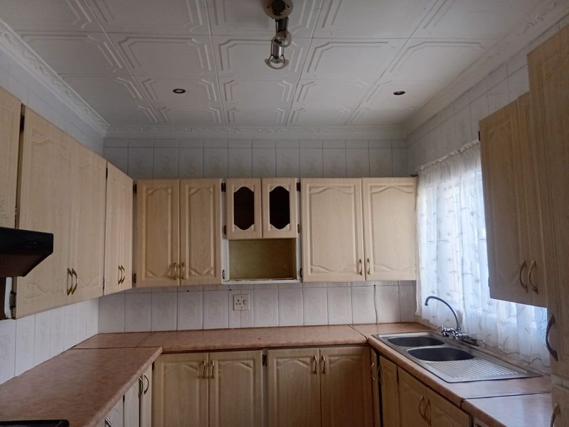 A dated kitchen featuring laminate cabinetry, a double bowl stainless steel sink, and decorative ceiling tiles, offering potential for a modern renovation.
