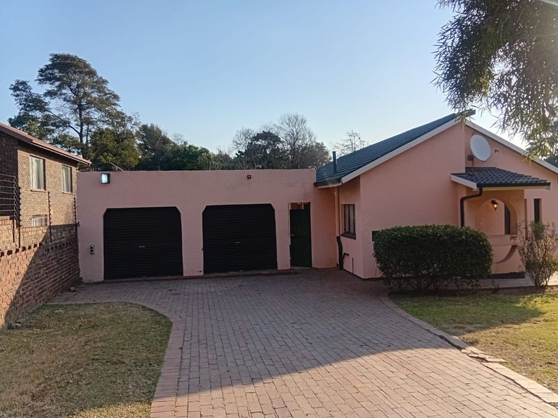 Front view of a residential property featuring a double garage, paved driveway, and brick boundary wall with a tiled roof structure.