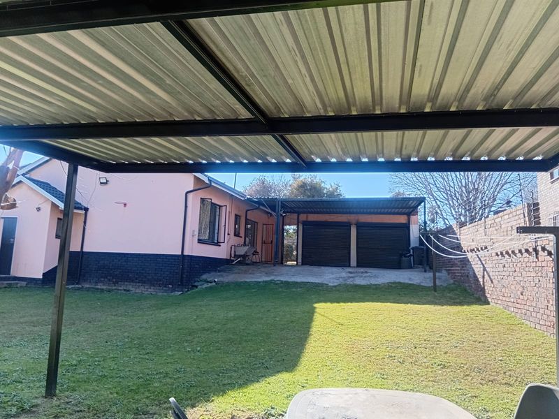 Rear exterior view featuring a lawn, a double garage with a carport, and a brick boundary wall.