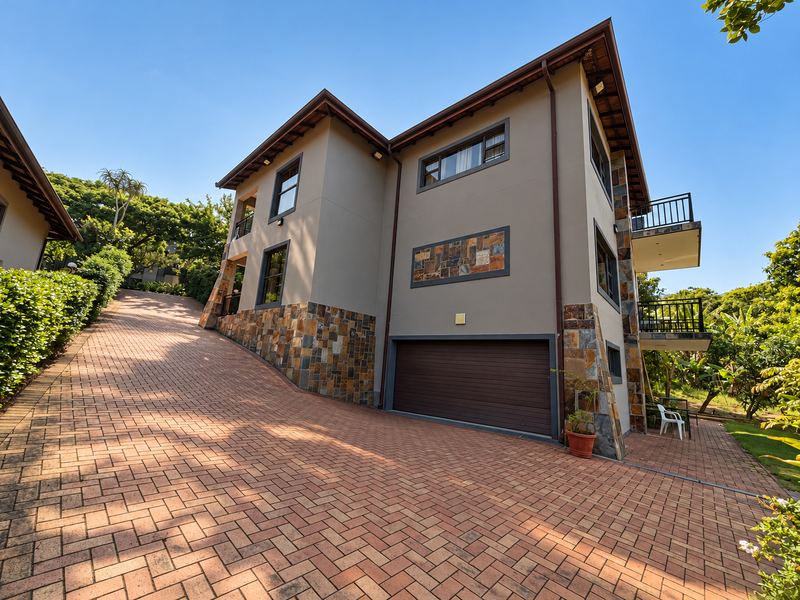 A well-maintained multi-story residence featuring stone cladding, a spacious brick-paved driveway, an integrated garage, and private balconies.