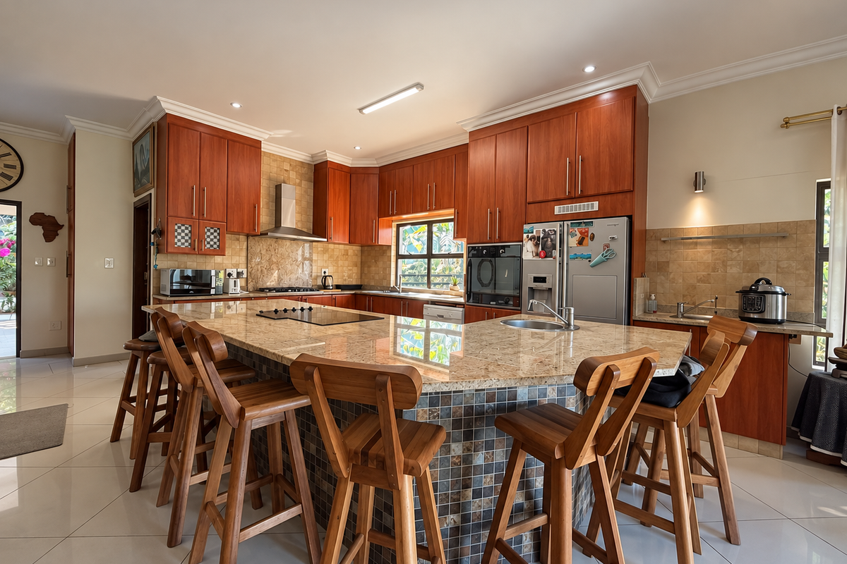 Spacious kitchen featuring warm wood cabinetry, granite countertops, a large central island with seating, and integrated appliances, finished with neutral floor tiles.