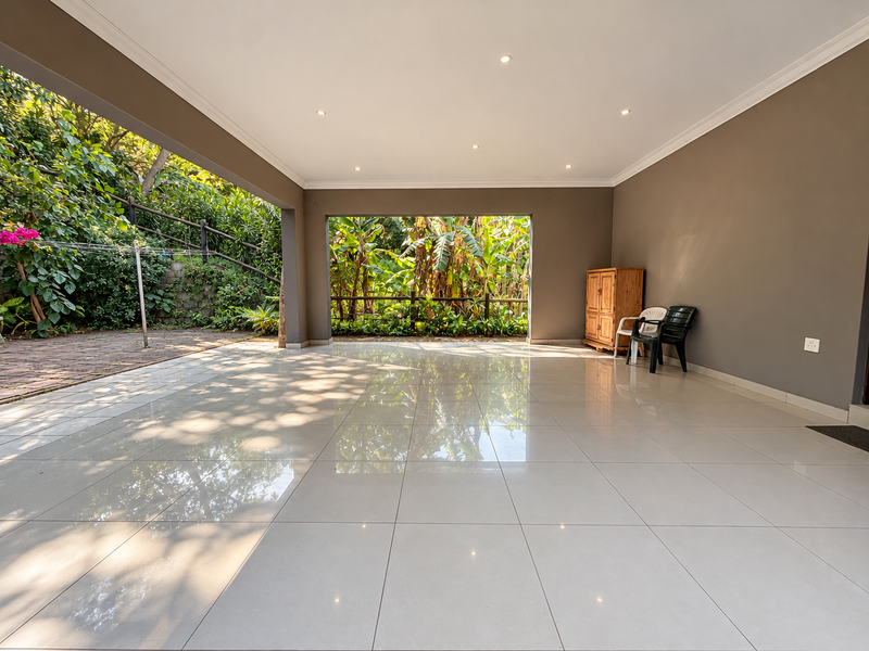Spacious covered patio featuring polished tiled flooring, recessed downlighting, and direct access to a lush garden area.
