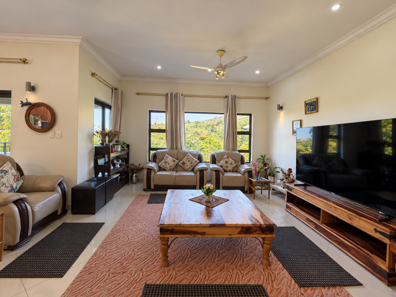 A bright and spacious living room featuring large windows with scenic views, tiled flooring, recessed lighting, and a ceiling fan.
